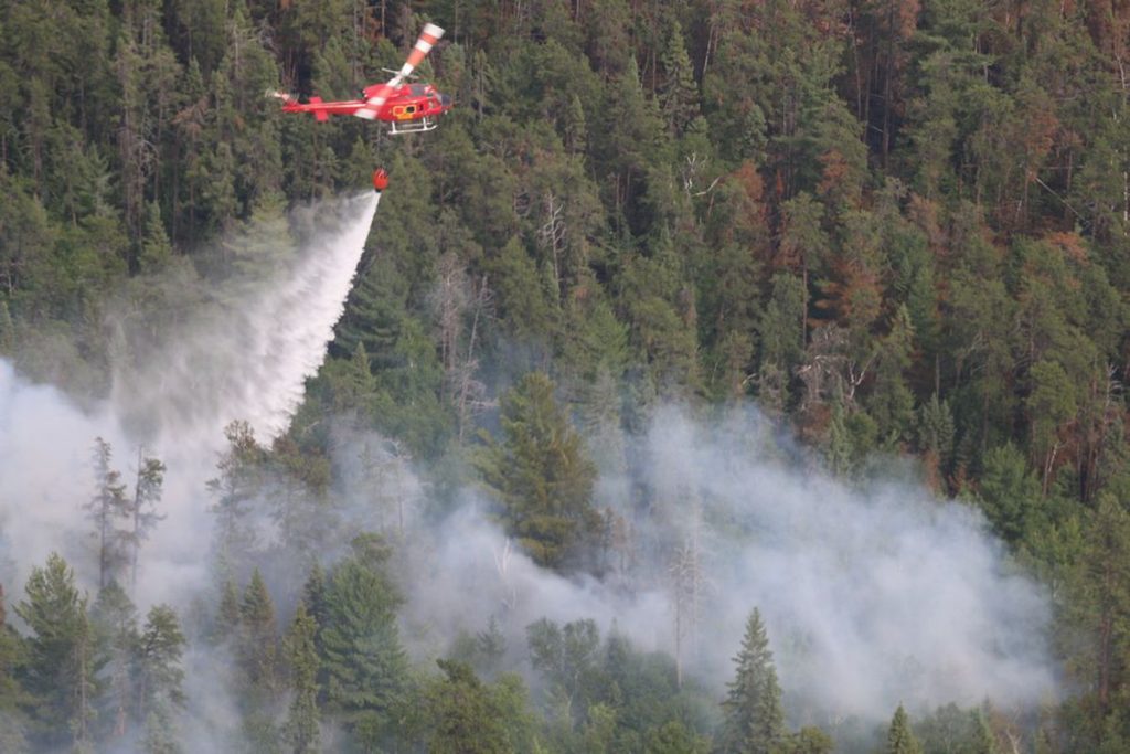 a helicopter with bucket dropping water on a wildfire